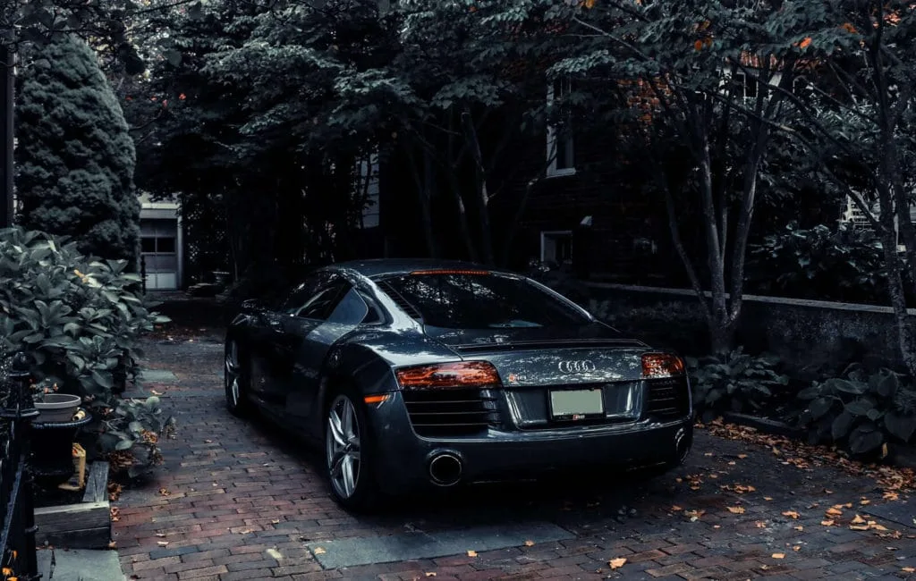 A dark grey sports car parked on a brick driveway under trees